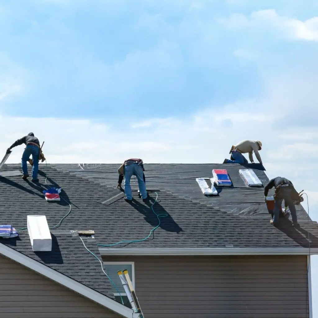 four men working on an asphalt shingle roof