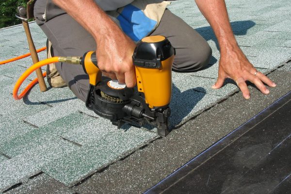 Roofer uses nail gun to attach asphalt shingles to roof